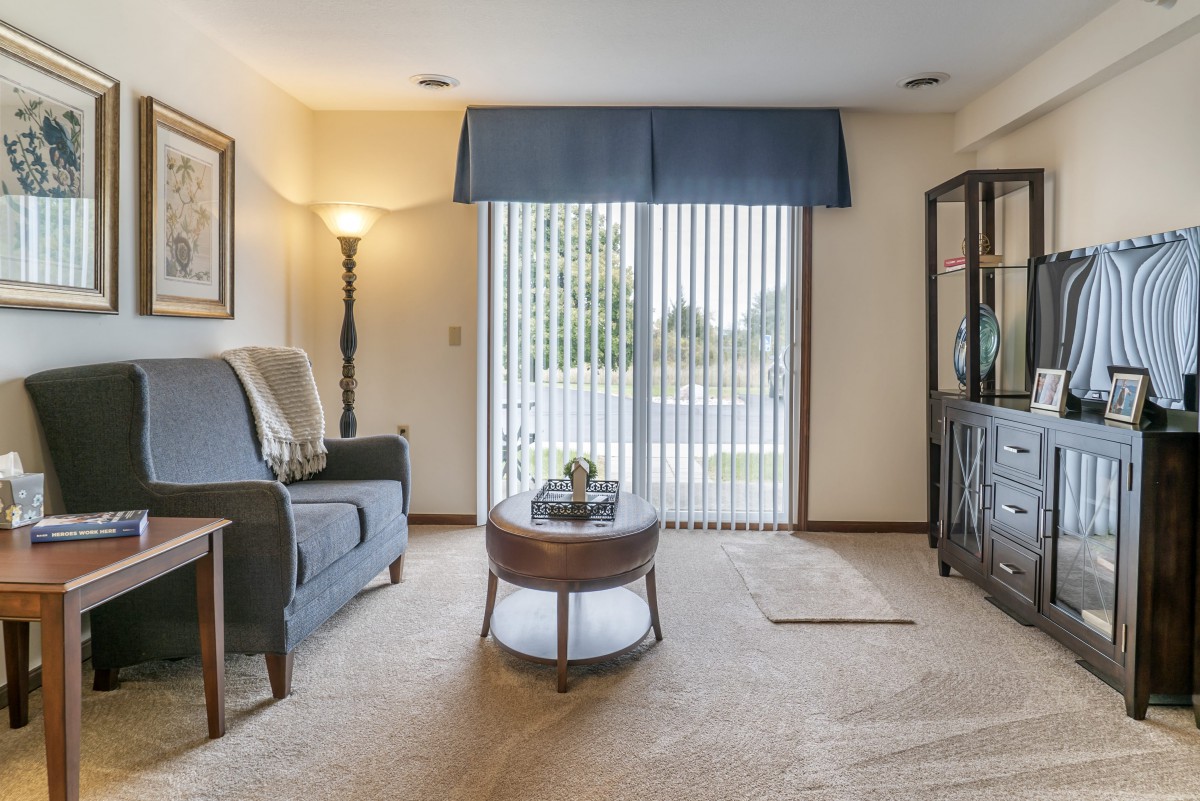 A cozy living room featuring a sofa, coffee table, and floor lamp, with a view through sliding glass doors.