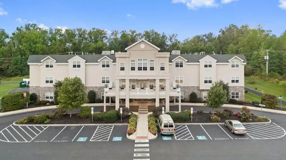 A large building with an ornate entrance and a parking lot in front, surrounded by trees under a clear blue sky.
