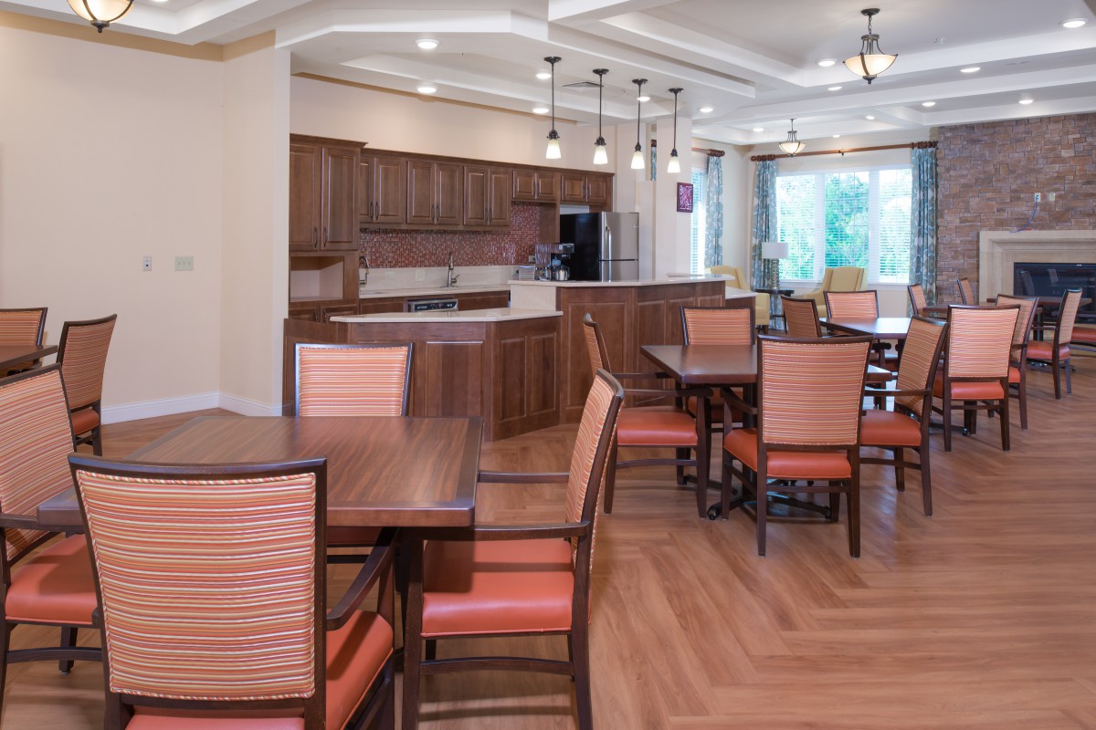A modern dining and kitchen area with wooden tables and chairs, pendant lighting, and a hardwood floor.