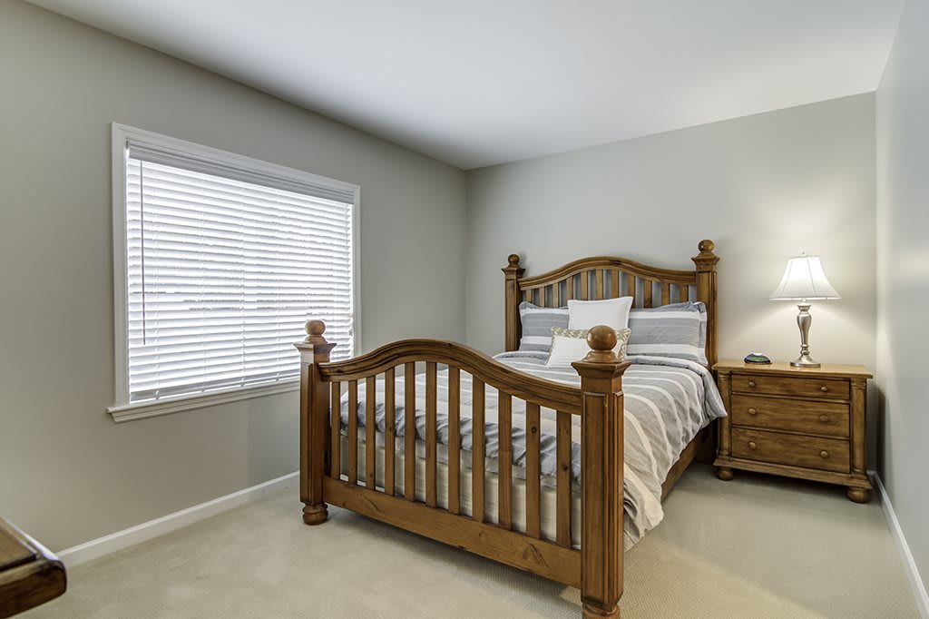 A cozy bedroom with a wooden bed frame, striped bedding, and a nightstand beside a window.