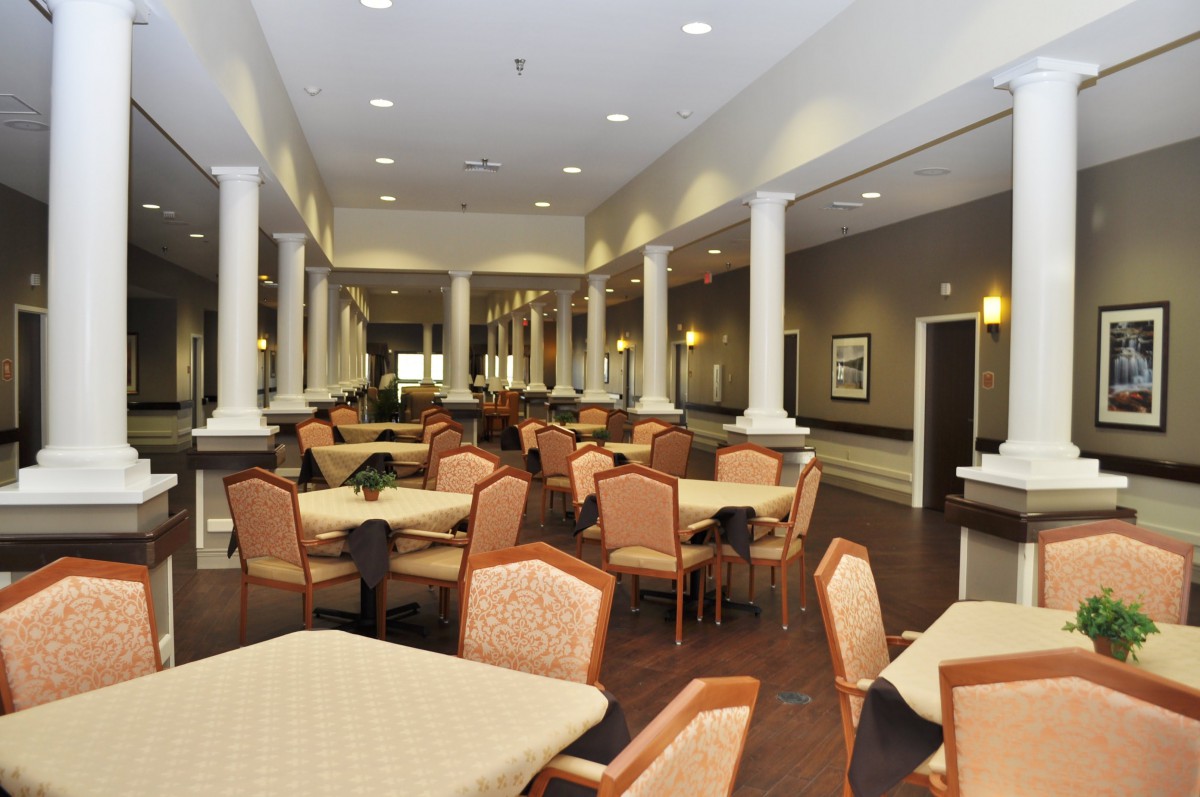 An elegant dining area featuring neatly arranged tables and chairs, illuminated by soft lighting and adorned with classical columns.