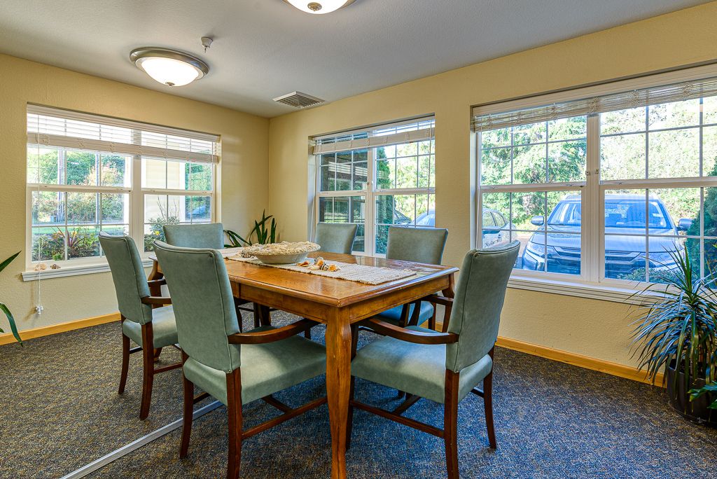 A cozy dining room with a wooden table and chairs, illuminated by natural light through large windows.