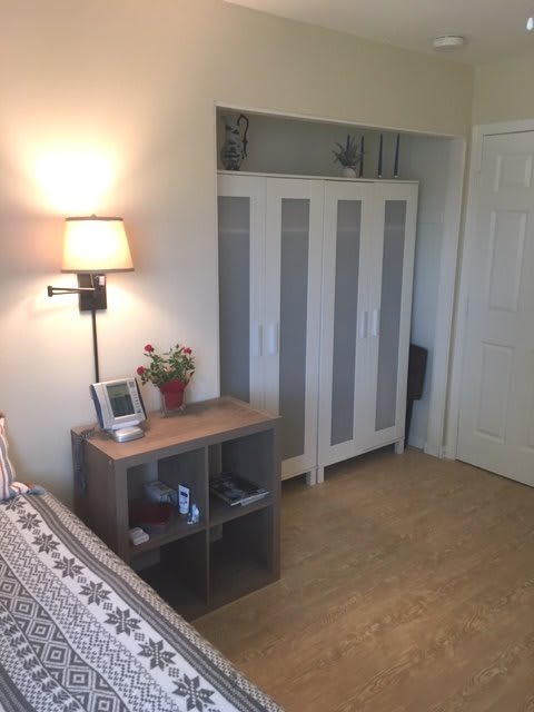 A minimalist bedroom featuring a wardrobe, small shelf with decorations, and a wall-mounted lamp.