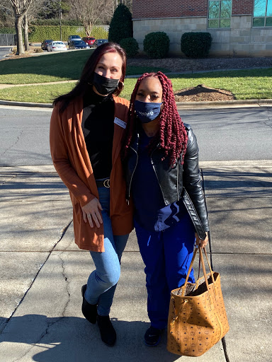 Two friends posing together outdoors, both wearing masks and casual outfits.