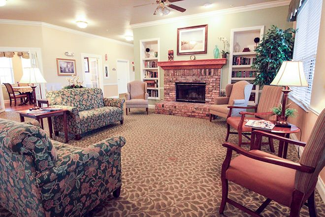 A cozy living room featuring a fireplace, surrounding sofas and chairs, and bookshelves lining the walls.