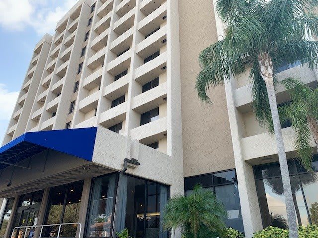 A multi-story hotel building with a blue awning at the entrance and palm trees nearby.