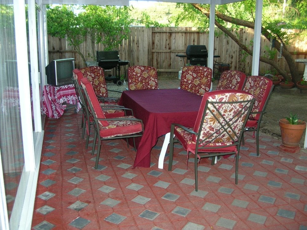 An outdoor patio with a dining set featuring a table covered with a burgundy cloth and chairs with patterned cushions.