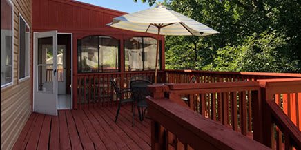 A cozy outdoor patio with a table and chairs under a large umbrella, surrounded by trees.