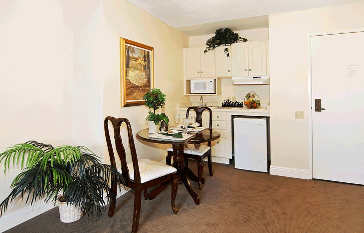 A cozy dining area with a small kitchenette, featuring a table and chairs, elegantly decorated with plants and artwork.