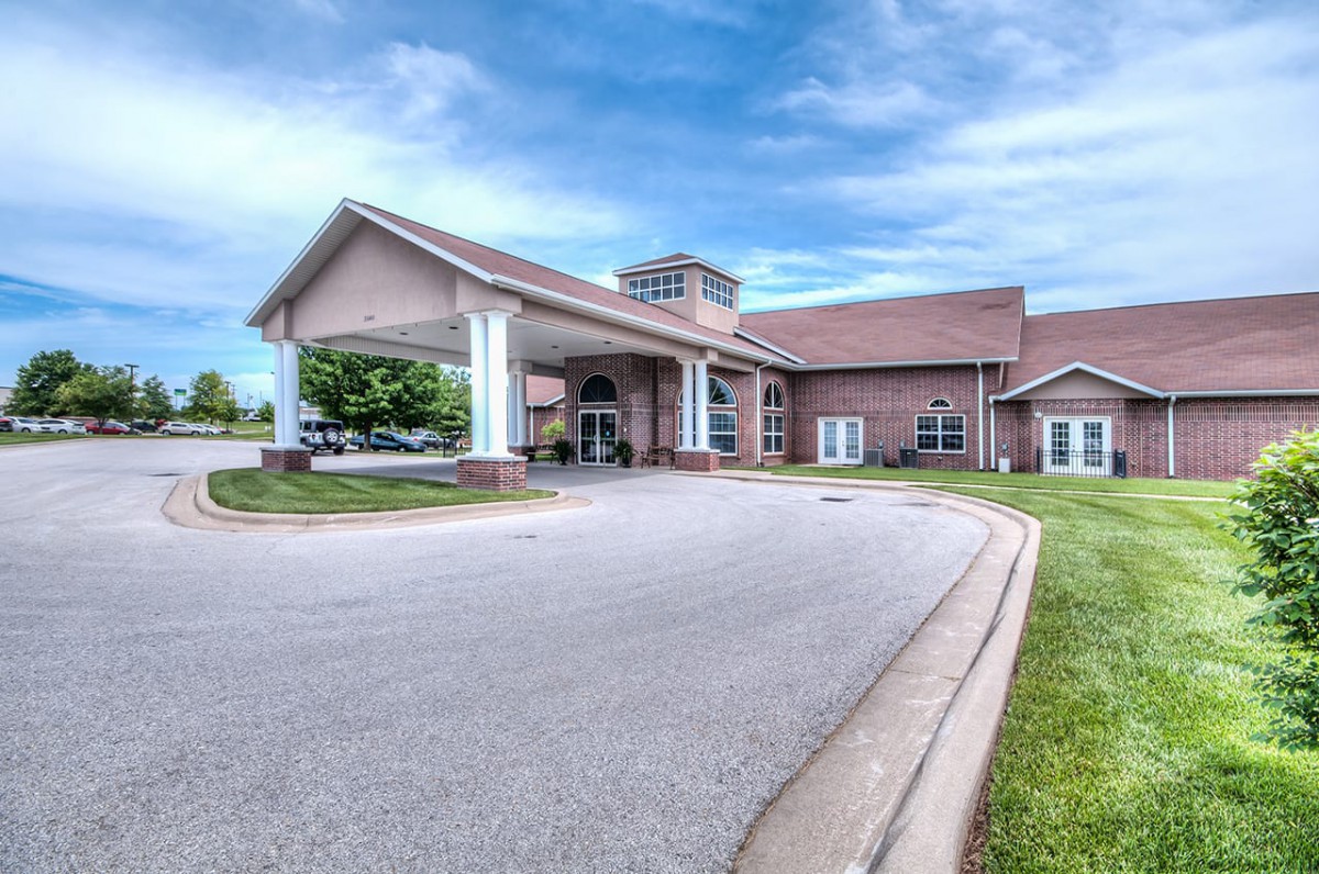 A modern building with a covered entrance and spacious driveway under a partly cloudy sky.