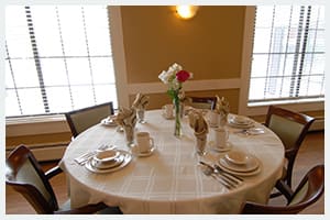 A neatly set dining table with plates, utensils, and a flower vase as the centerpiece.