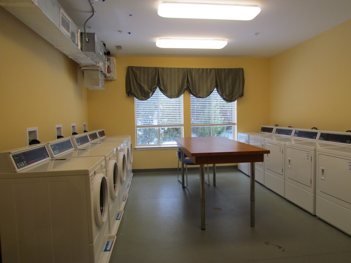 A laundry room with multiple washing machines and dryers, featuring a central folding table.