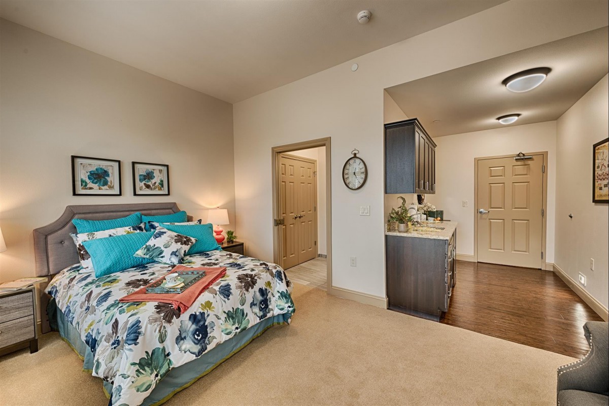 A cozy bedroom with a neatly made bed and attached kitchenette.