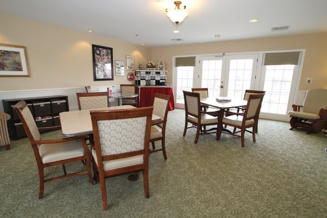 A well-lit dining area with multiple tables and chairs arranged neatly on a carpeted floor.