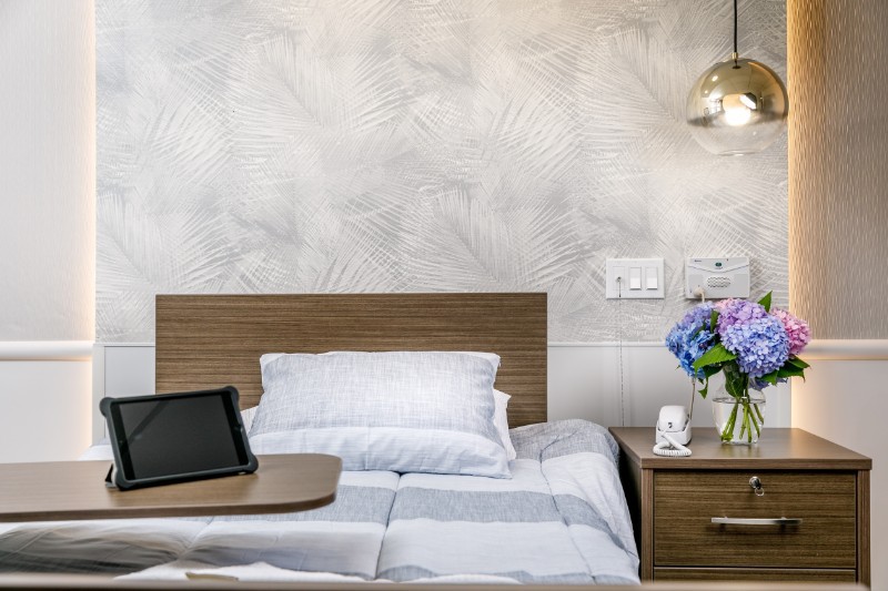 A cozy bedroom with a neatly made bed, a nightstand with flowers, and a modern lamp.