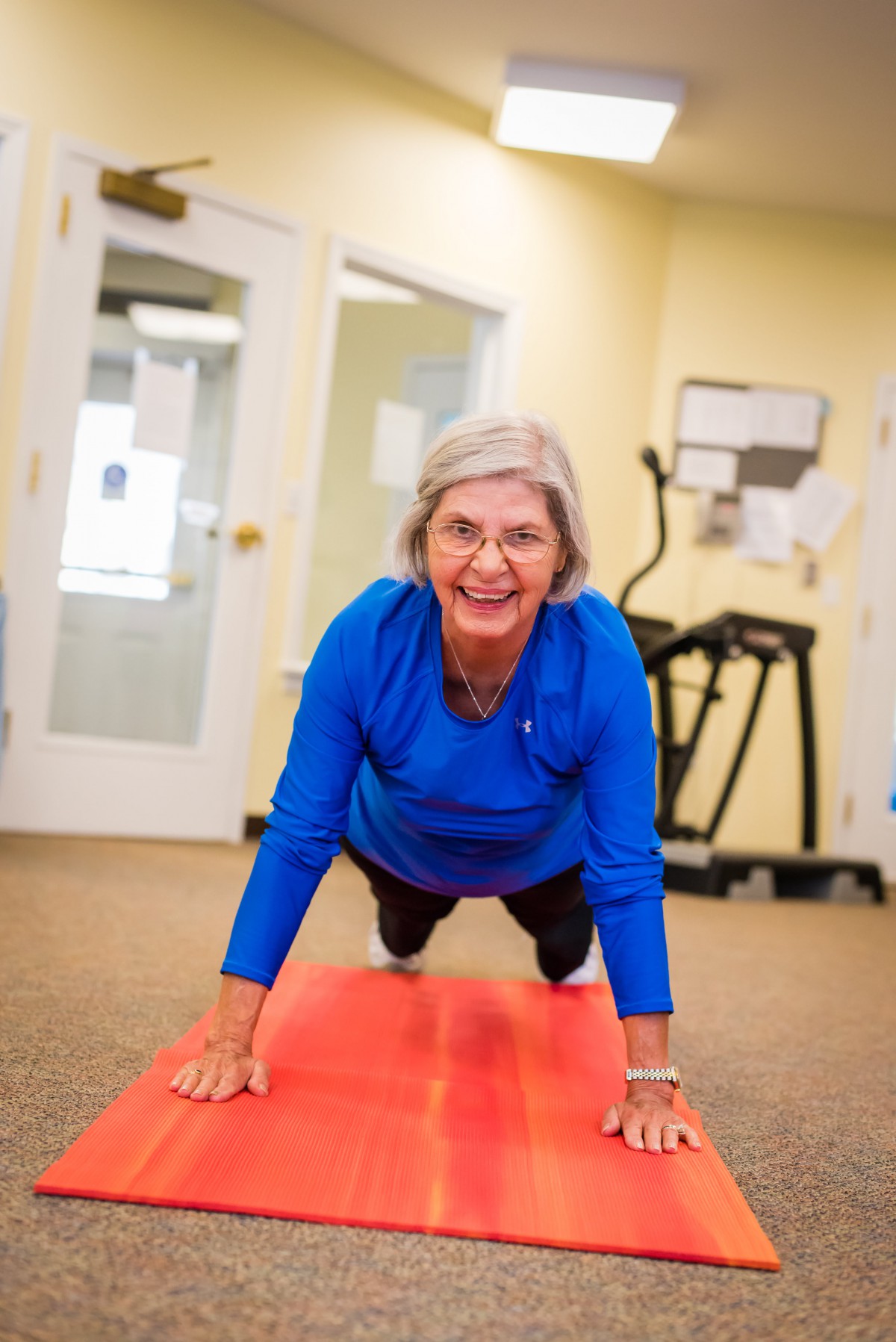 An elderly woman exercising on a yoga mat indoors, performing a plank pose.