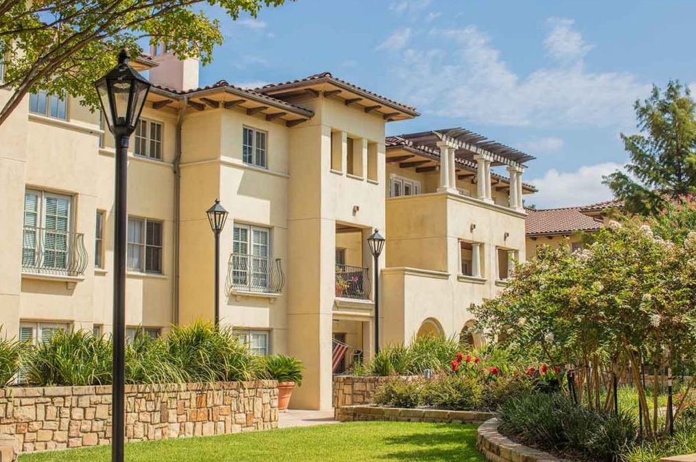 A modern residential apartment building surrounded by a well-maintained garden on a sunny day.