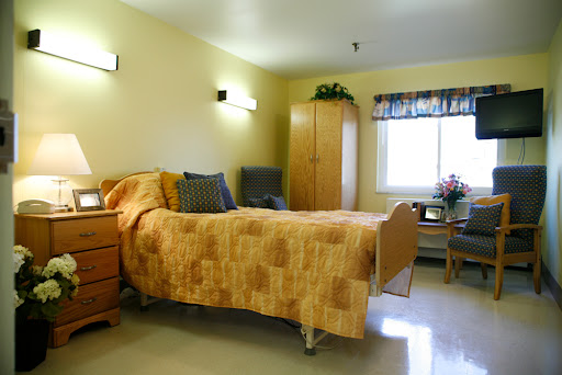 A cozy hospital room featuring a single bed, a wardrobe, and natural light coming through the window.