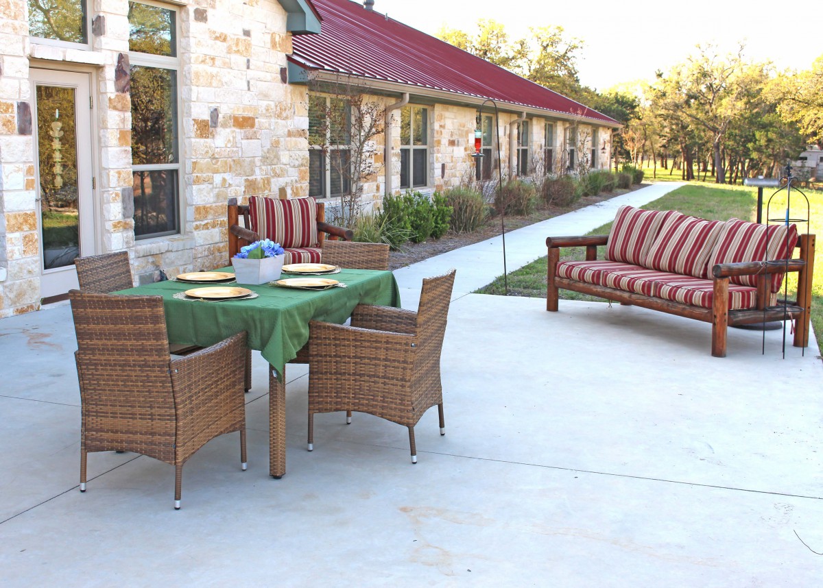 A well-furnished patio area with a table, chairs, and sofa beside a stone building with a red roof.