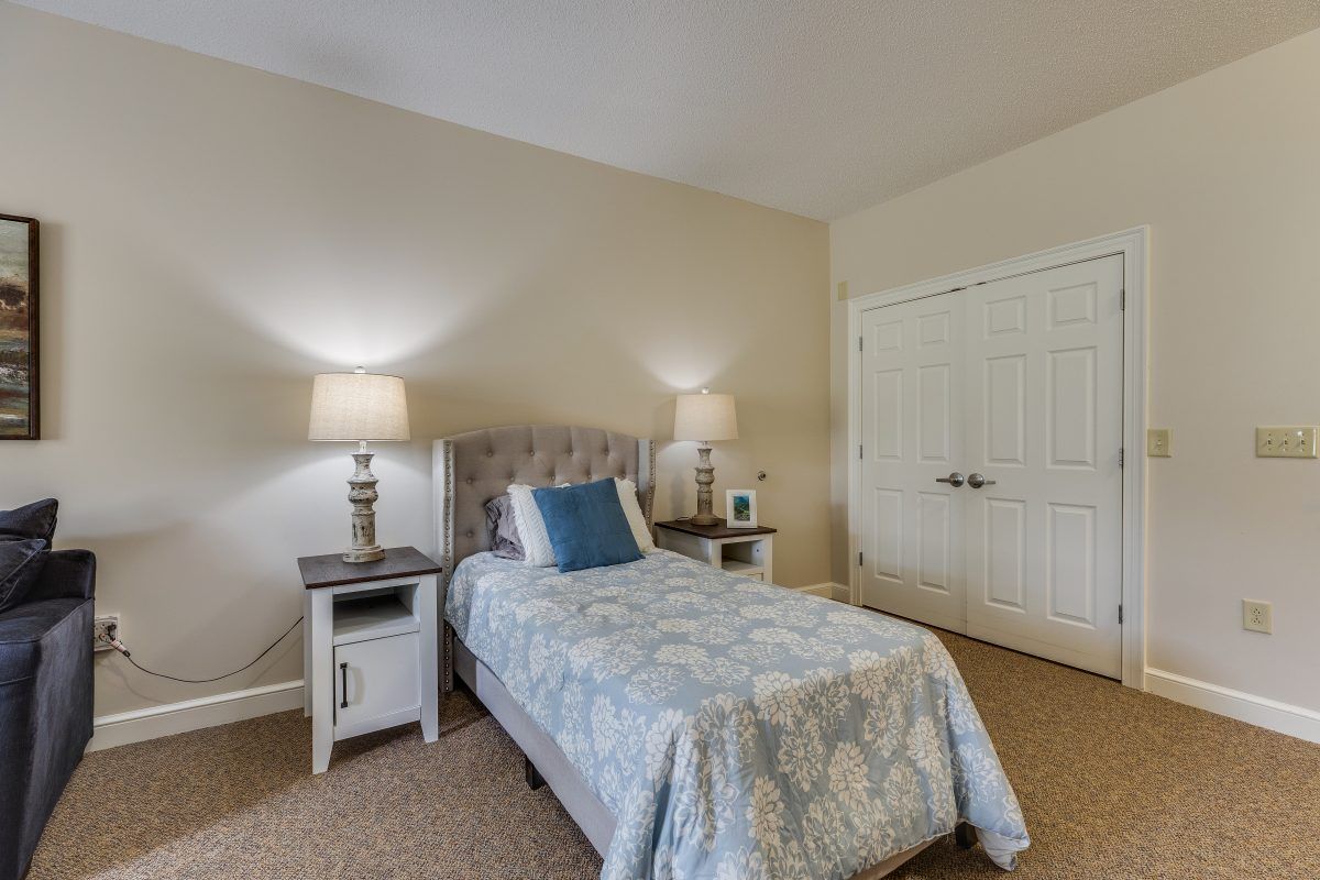 A cozy bedroom featuring a single bed with a decorative quilt, flanked by two nightstands and lamps, all set on a carpeted floor.