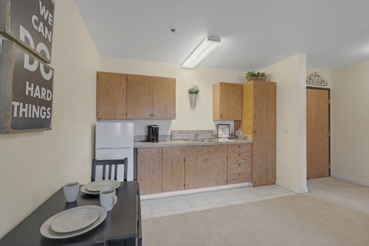 A minimalist kitchen with wooden cabinets, a small refrigerator, and a dining table set for two.