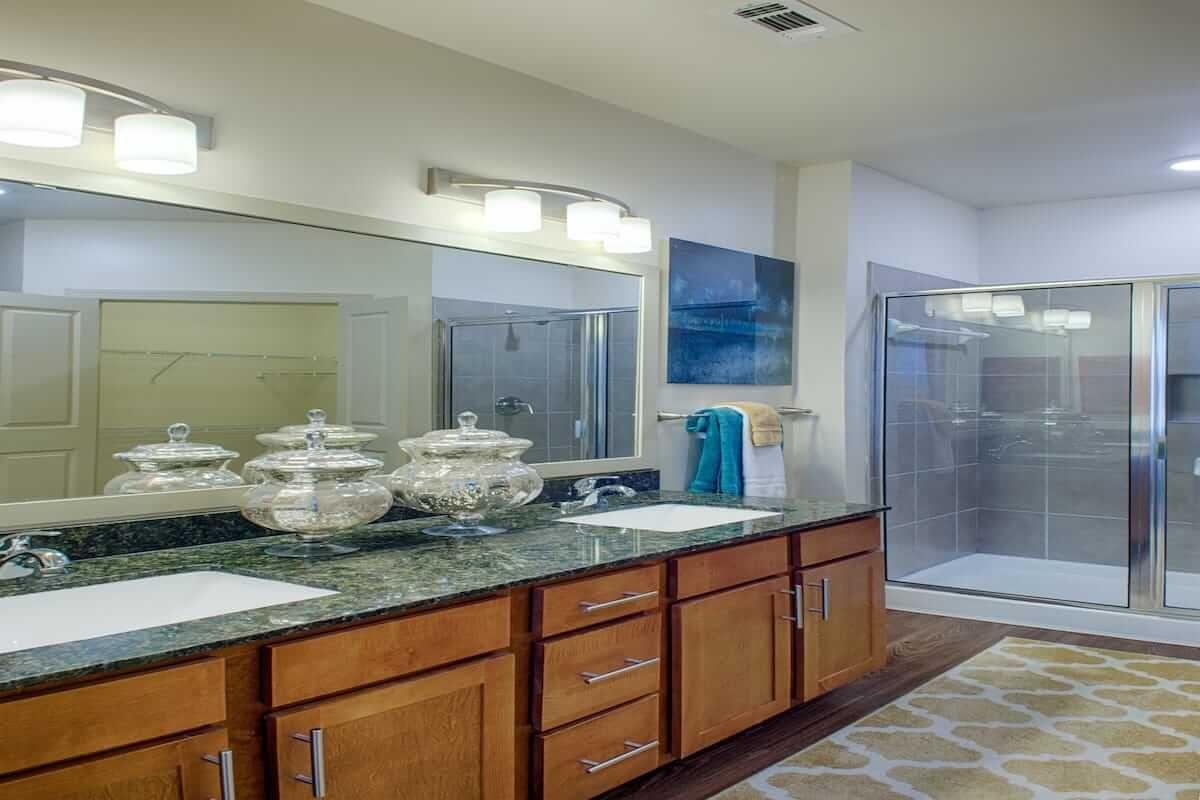 A modern bathroom with a double vanity, large mirror, and walk-in shower.