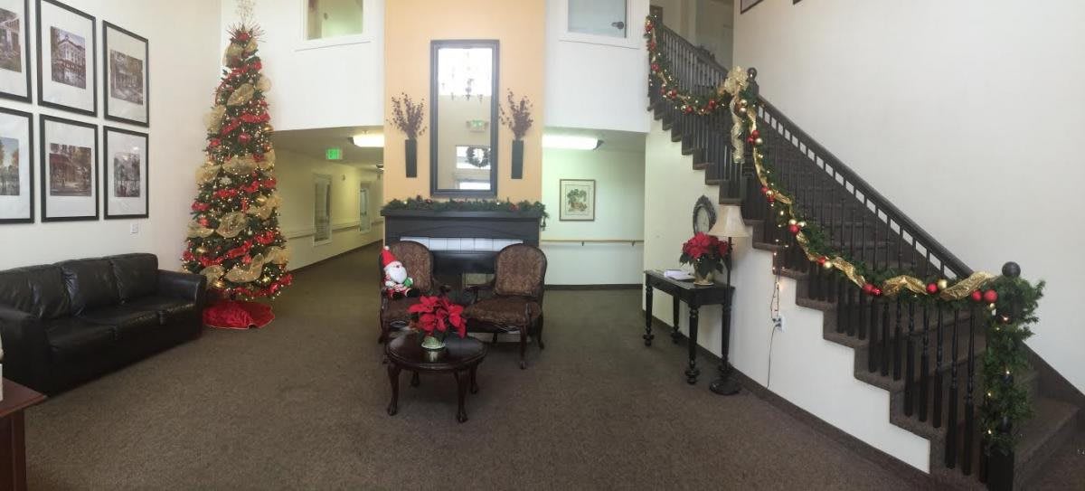 A cozy lobby decorated for the holidays with chairs, a table, poinsettias, and a staircase adorned with garlands.