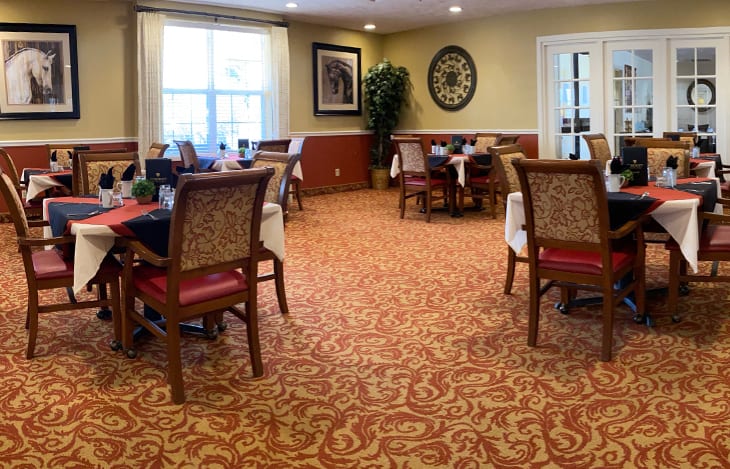 A well-decorated dining room with multiple tables and chairs, featuring elegant carpeting and wall decor.