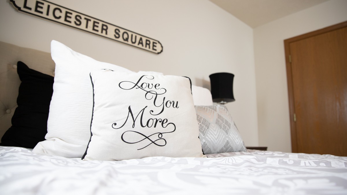 A cozy bedroom featuring a decorative pillow with the text 'Love You More'.