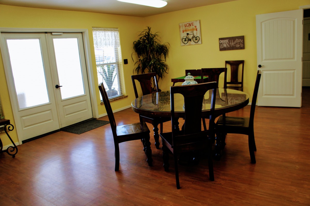 A cozy dining room with a round wooden table and chairs, featuring yellow walls, wall art, and an indoor plant.