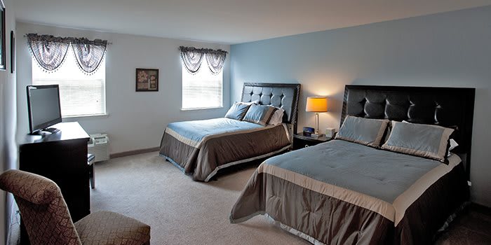 A cozy bedroom with two beds, a lamp, and a window allowing natural light.