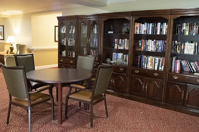 A cozy reading room featuring a wooden bookshelf and a table surrounded by chairs.