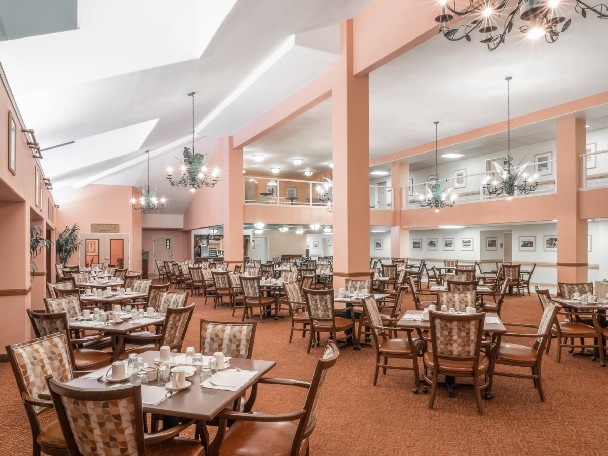A spacious and elegant dining room with neatly arranged tables and chairs, illuminated by chandeliers.