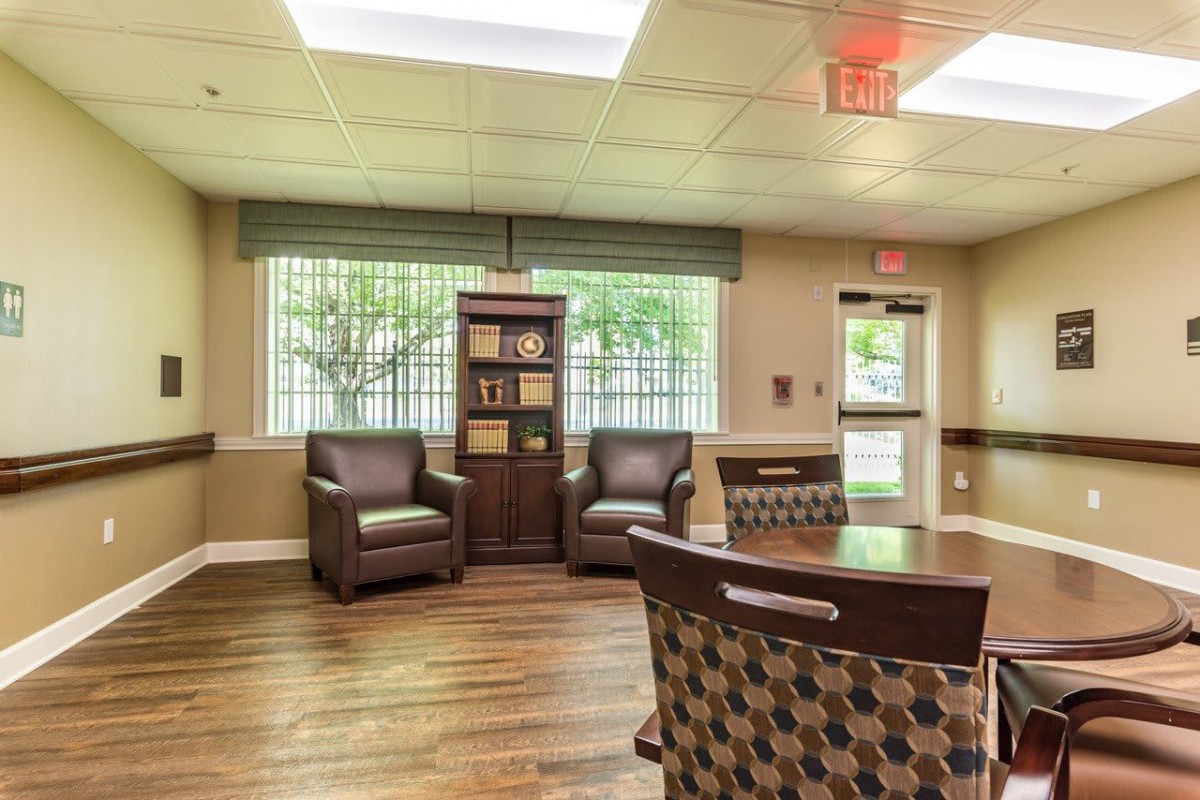 A cozy waiting room featuring comfortable chairs, a bookshelf, and large windows.