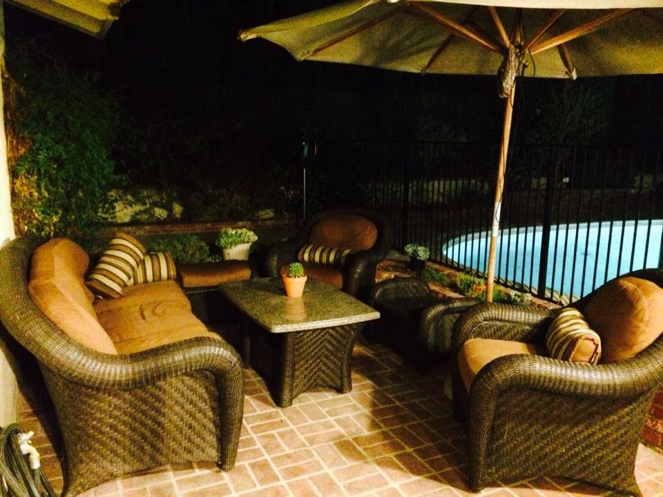 A cozy outdoor patio seating area at night, featuring wicker furniture and an umbrella by the pool.