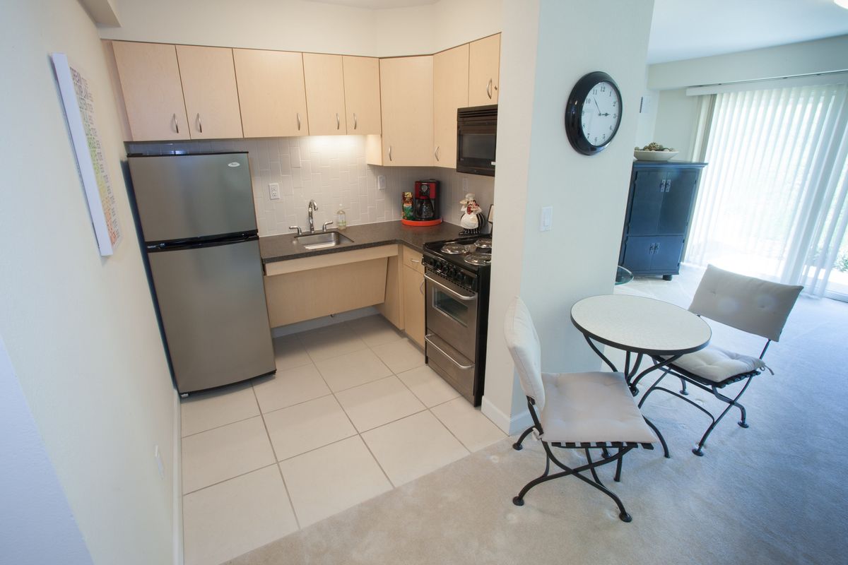 A compact, modern kitchen with light wood cabinets and stainless steel appliances.