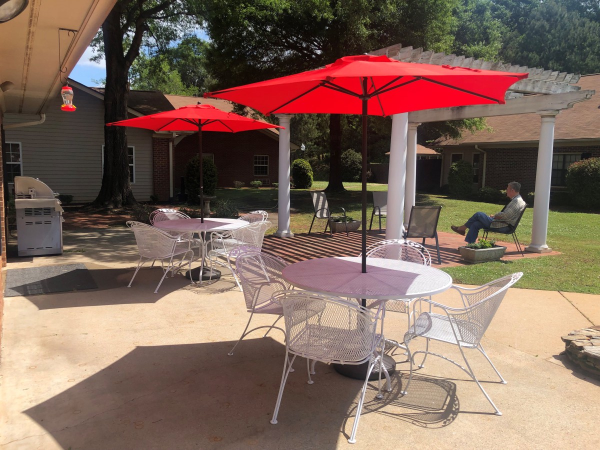 A sunny outdoor patio area with tables, chairs, and red umbrellas.