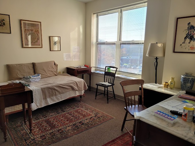 A cozy bedroom with a large window, various furniture items, and natural light streaming in.