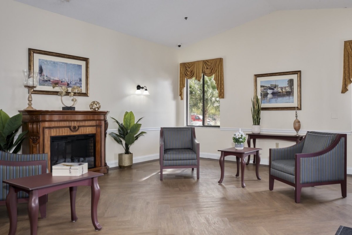 A cozy living room with classic furnishings, including armchairs, a fireplace, and decorative plants.