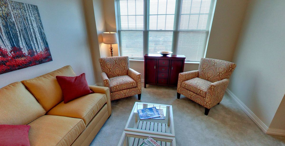 A cozy living room with a sofa, two armchairs, a lamp, and a small cabinet by the window.