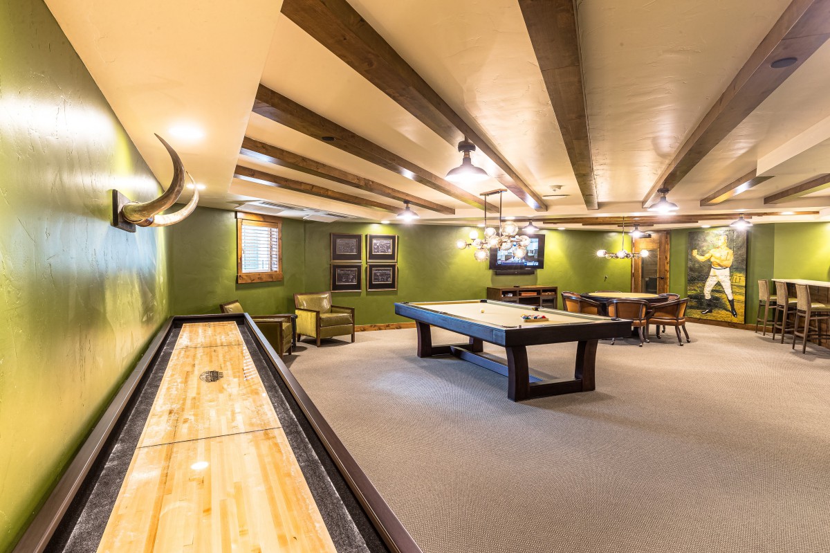 A cozy game room featuring a pool table and shuffleboard under warm lighting.