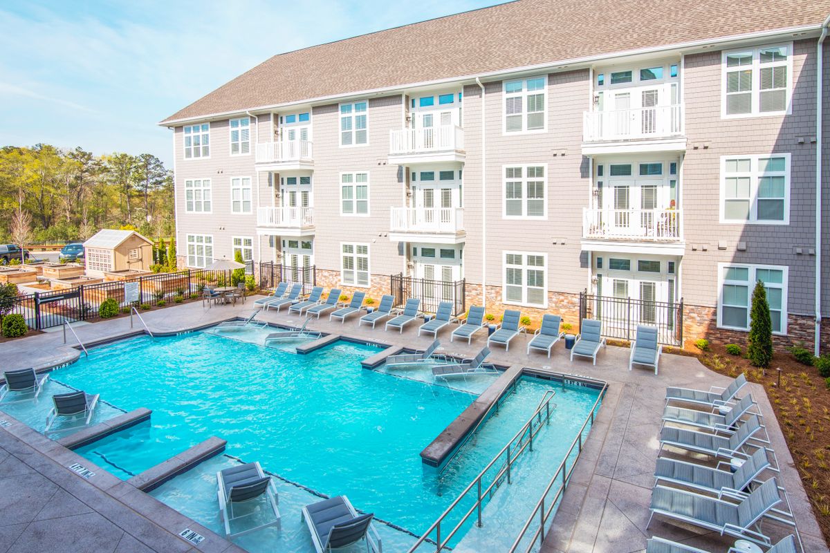 A modern apartment complex with an outdoor swimming pool surrounded by loungers.