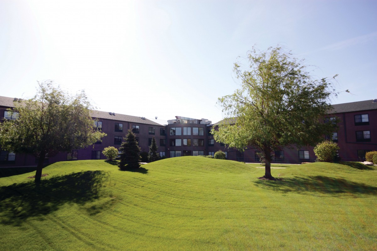 A scenic view of a building with a well-maintained lawn and trees under a clear sky.