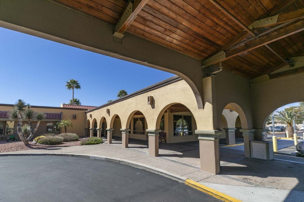 A sunny view of a building exterior featuring arches and palm trees.