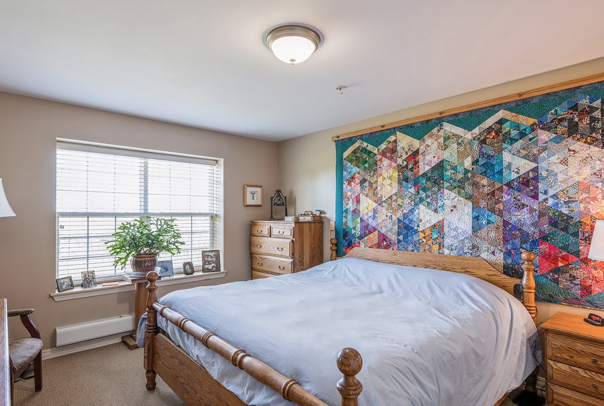 A cozy bedroom with a wooden bed and a colorful quilt hanging on the wall.