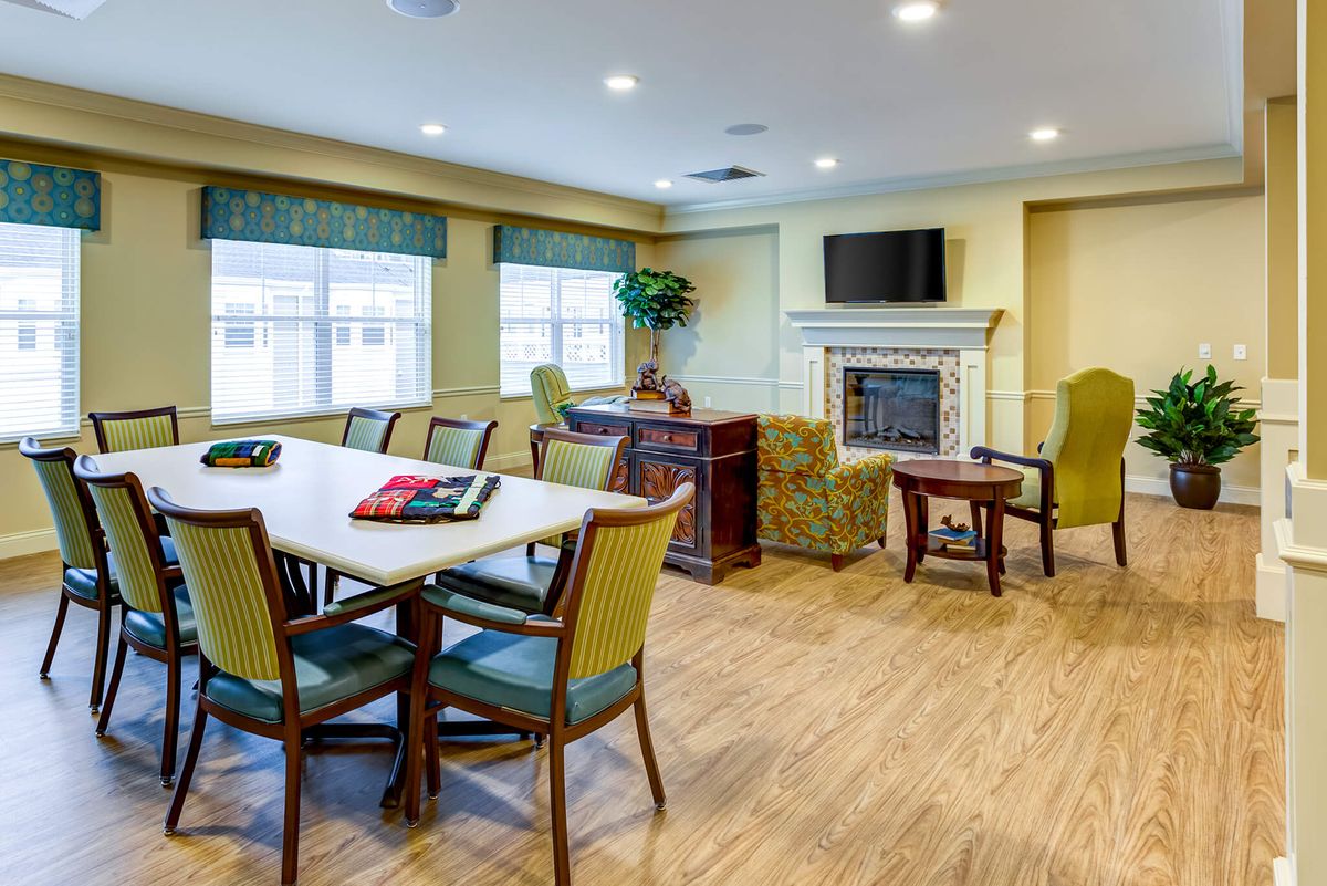 A well-lit meeting room with a conference table, chairs, and a fireplace beneath a television.