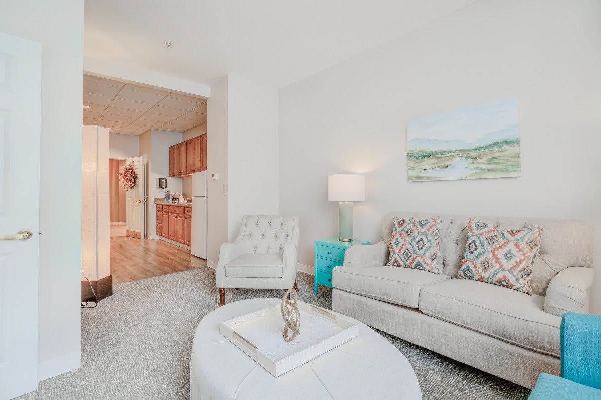 A cozy living room with a view into the kitchen, featuring a comfortable sofa, a stylish lamp, and wall art.