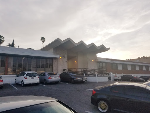 A modern building with a unique roof design, surrounded by parked cars during sunset.