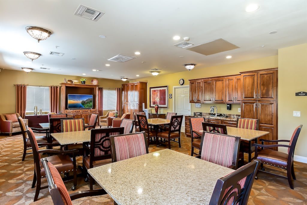 A well-lit dining area featuring multiple tables and chairs, with a kitchen space in the background.