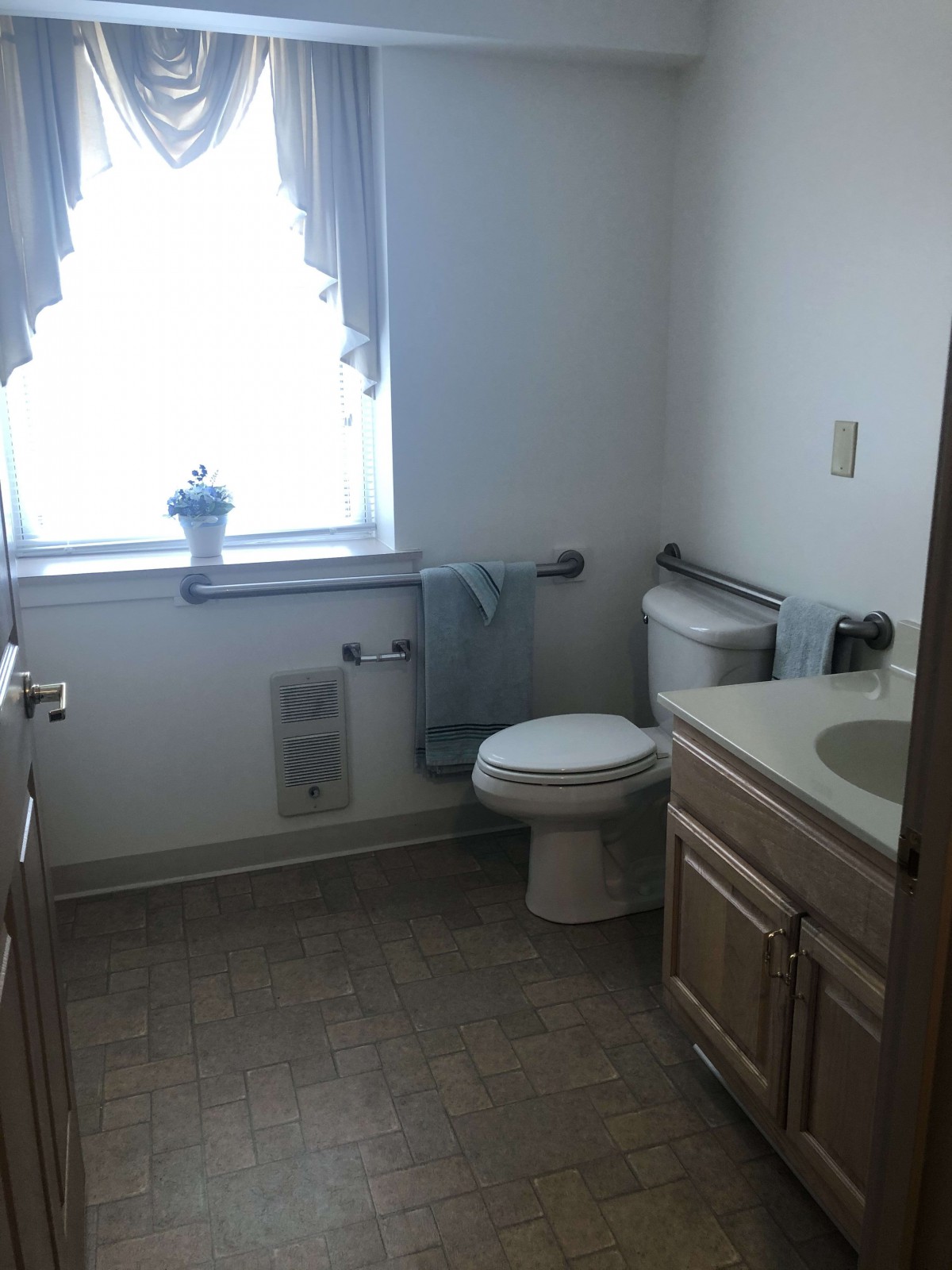 A bright bathroom with a toilet, sink, and neatly arranged towels by the window.